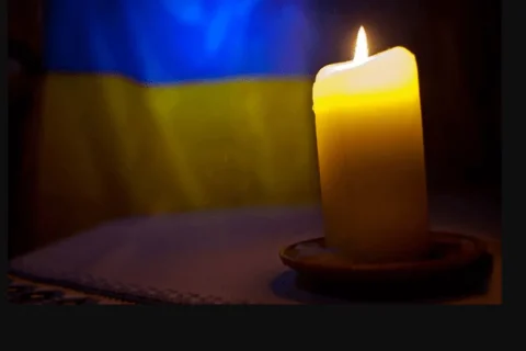 Запалена жовта свічка на блюдці на тлі синьо-жовтого прапора України