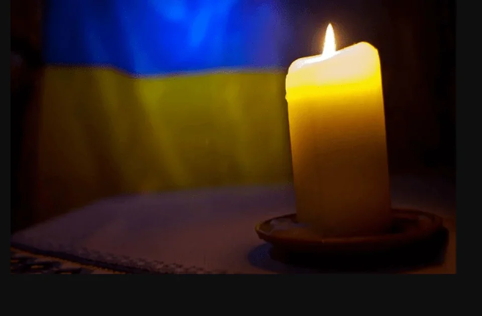 Запалена жовта свічка на блюдці на тлі синьо-жовтого прапора України