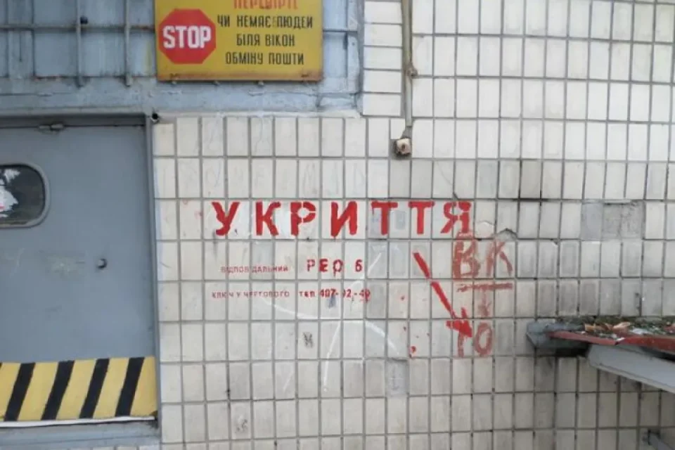 Червоний напис Укриття на плитці біля сірих дверей і жовтої таблички STOP