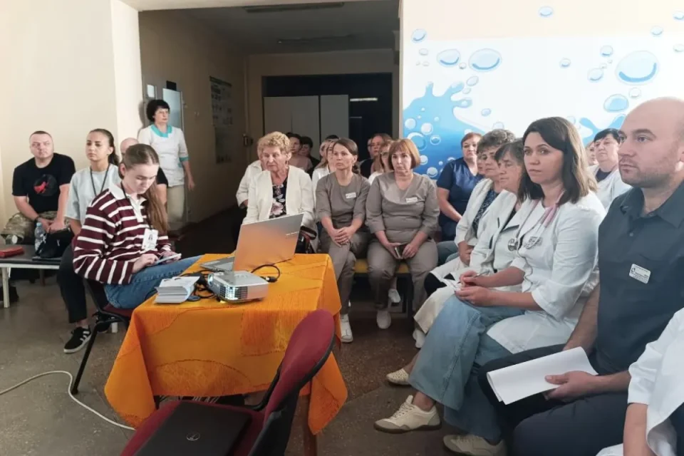 Медики сидять на нараді біля ноутбука і проєктора в залі поліклініки